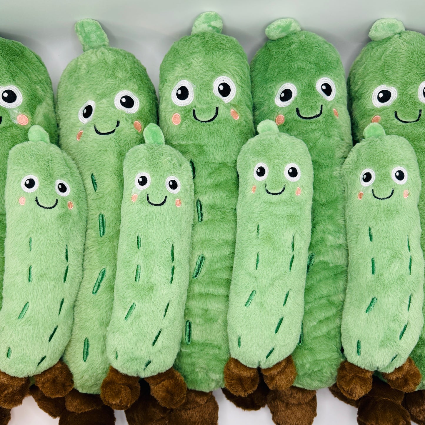 Row of plush cucumber pickle toys with smiling faces on a white background