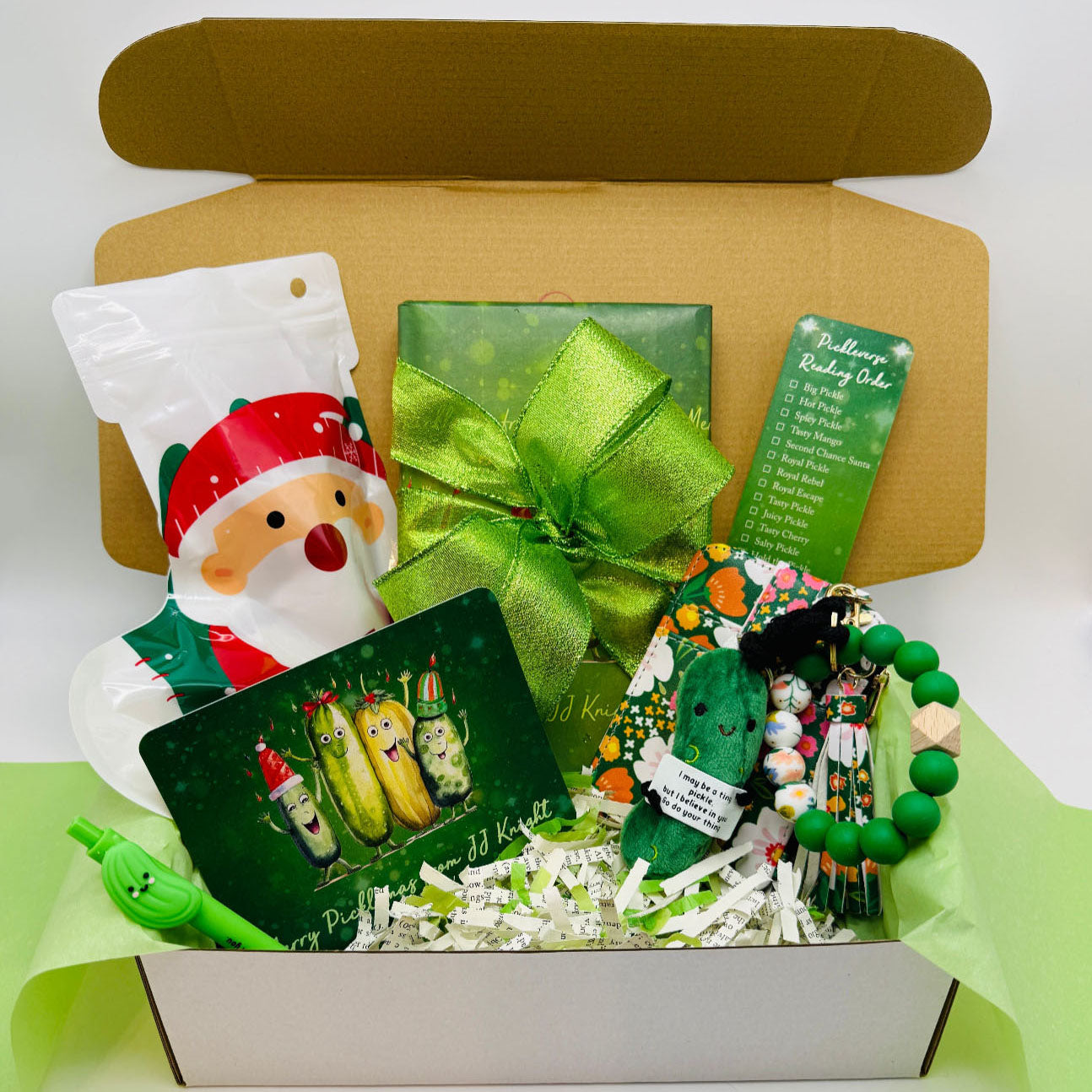Christmas Pickle gift box with green ribbon, Santa Claus-themed item, and decorative items with wrapped romantic comedy book
