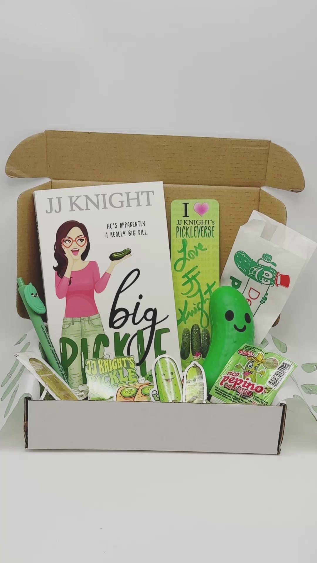 JJ Knight pickle-themed product set including a full length romantic comedy paperback, a stress pickle, keychain, stickers, and packaging 