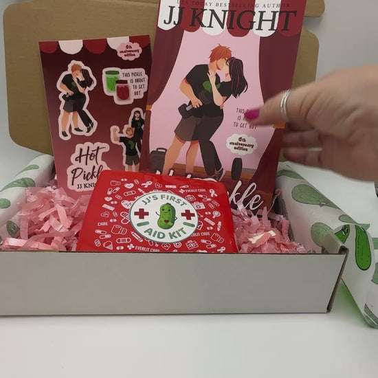 A curated gift box set featuring a copy of the book 'Hot Pickle' by JJ Knight, a red 'First Aid Kit' box, and matching stickers.