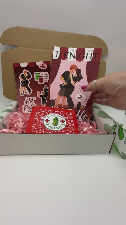 A curated gift box set featuring a copy of the book 'Hot Pickle' by JJ Knight, a red 'First Aid Kit' box, and matching stickers.